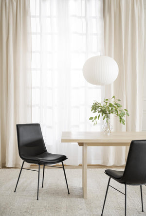 Svarta lädersstolar vid ljust matbord med vit taklampa och beige gardiner i modern matsal