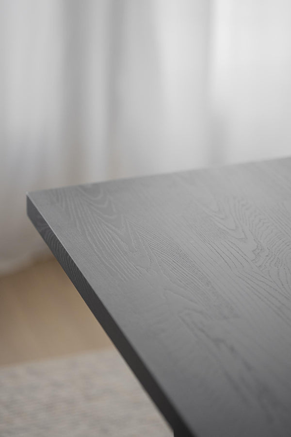 Grå bordsskiva i trä med synlig trästruktur och matt yta, närbild av hörn och kant