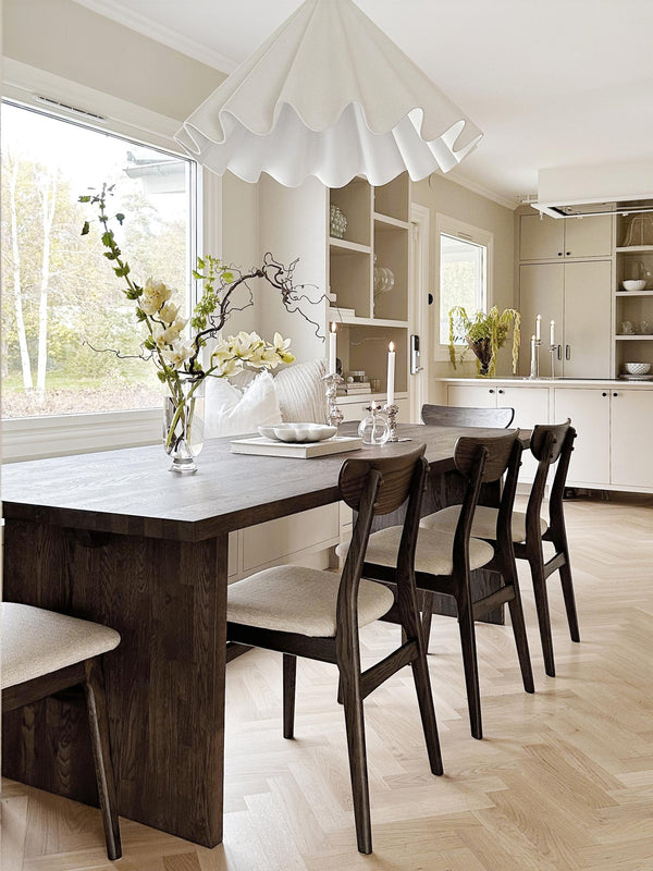 Ljust kök med matplats, mörkt matbord i trä, beigea stolar och vågformad taklampa