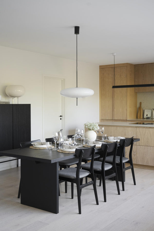 Matplats med svart matbord, svarta stolar och vit taklampa i modern skandinavisk stil