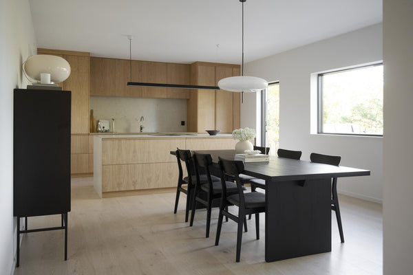 Minimalistiskt kök med ljust trä och svart matbord, moderna stolar och vit taklampa