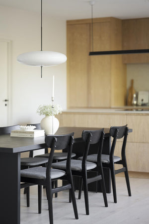 Matplats med svarta stolar och bord under vit taklampa i skandinaviskt kök med ljust trä