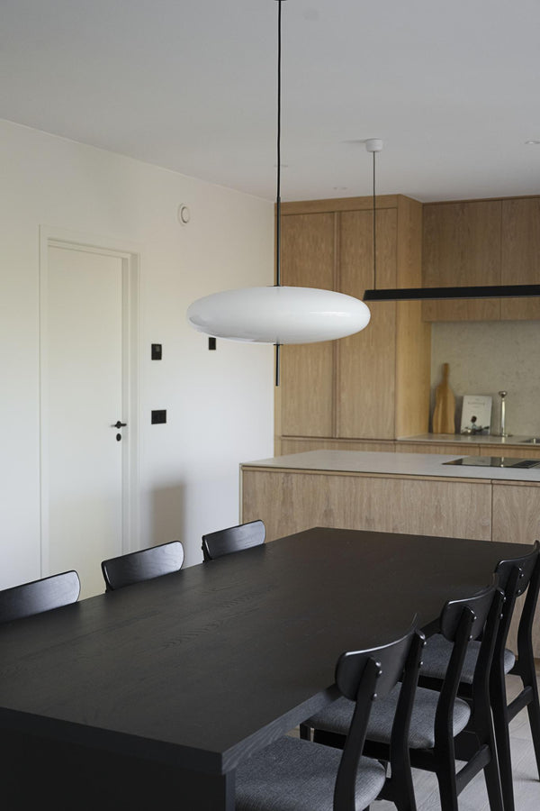 Modern taklampa i vitt glas med svart upphängning över matbord i skandinavisk köksmiljö