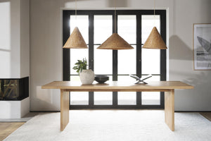 Matbord i ljust trä med tre rotting taklampar ovanför i modern matsal med svarta fönsterpartier