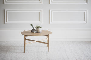 Runt soffbord i ljust trä med korsformade ben, dekorerat med växter i modern skandinavisk stil