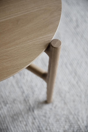 Närbild av träbord med rundat hörn och trästativ, elegant skandinavisk design mot ljus matta