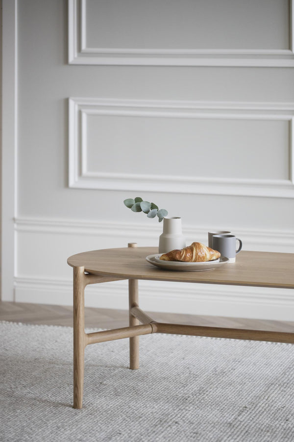 Runt soffbord i ljust trä med frukostuppläggning, vit vägginredning i bakgrunden