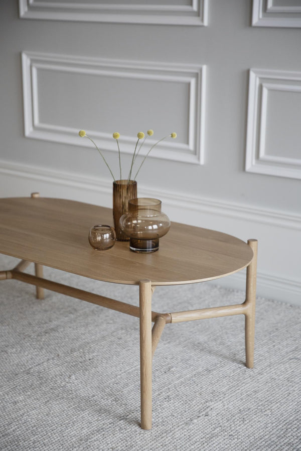 Ovalt soffbord i ljust trä med skandinavisk design, dekorerat med glasvaser på grå matta