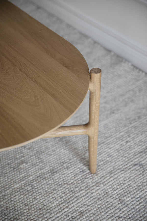 Närbild av trästol i ljus ek med organisk sits och runda ben på ljusgrå matta