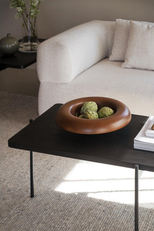 Terrakottafärgad dekorativ skål med gröna artiskockor på svart soffbord framför beige soffa