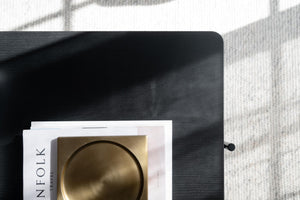 Svart träbricka med guldskål och inredningsmagasin på vit och grå rutad textil