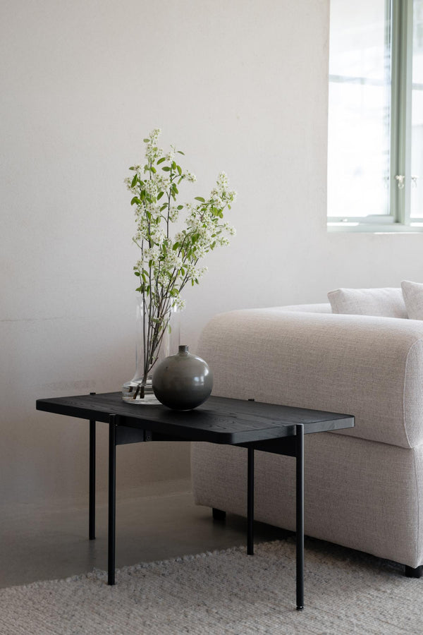 Svart soffbord med grön keramikvas och vita blommor i minimalistiskt vardagsrum med beige soffa