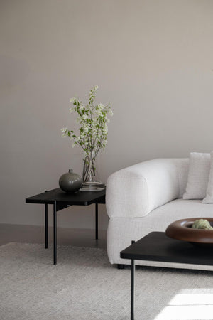 Ljust vardagsrum med beige soffa, svarta sidobord och vita blommor i vas mot neutral vägg