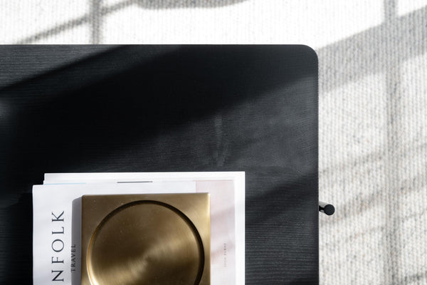 Svart träbricka med tidning och gyllene skål på ljust rutigt tyg