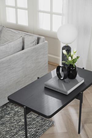 Sängbord i svart metall med lamp, vaser och böcker i minimalistiskt sovrum med grå textilier