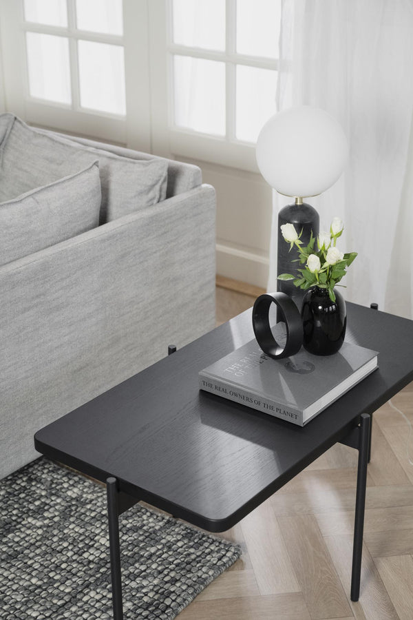 Sängbord i svart metall med lamp, vaser och böcker i minimalistiskt sovrum med grå textilier