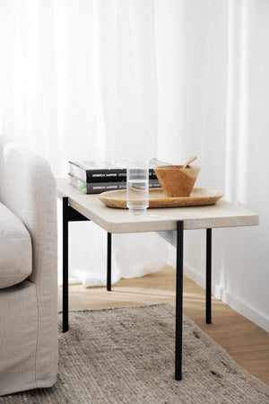 Ljust soffbord i trä med svarta ben, dekorerat med böcker, glas och träskålar bredvid beige soffa