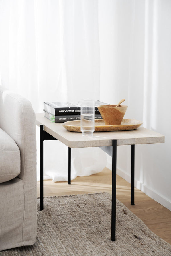 Ljust soffbord i trä med svarta ben, dekorerat med böcker, glas och träskålar bredvid beige soffa