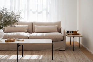 Beige soffa med ljusa kuddar och soffbord i ljust trä med svarta ben i minimalistiskt vardagsrum