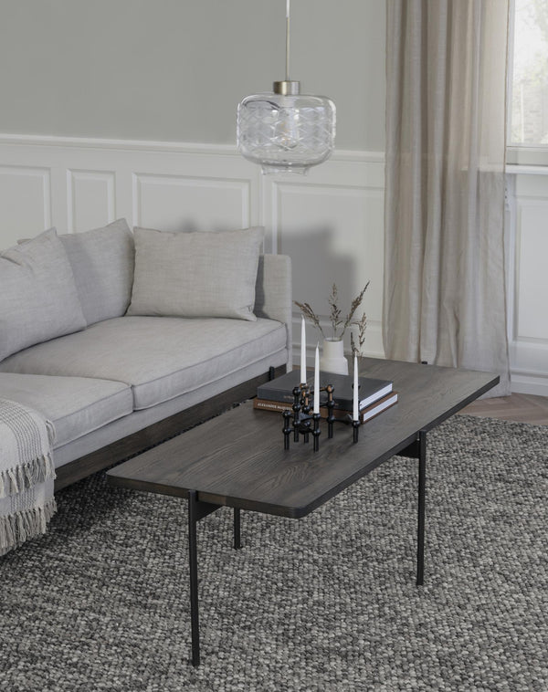 Modernt vardagsrum med grå soffa, svart soffbord med träskiva och glaspendel ovanför