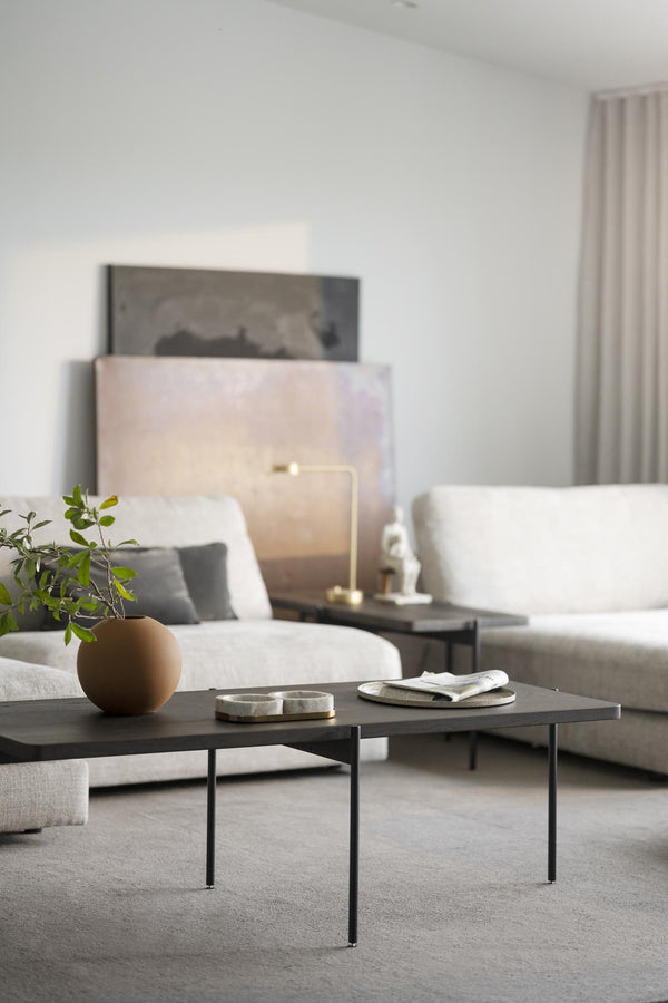 Minimalistiskt vardagsrum med grått soffbord, vit soffa och beige konst på väggen