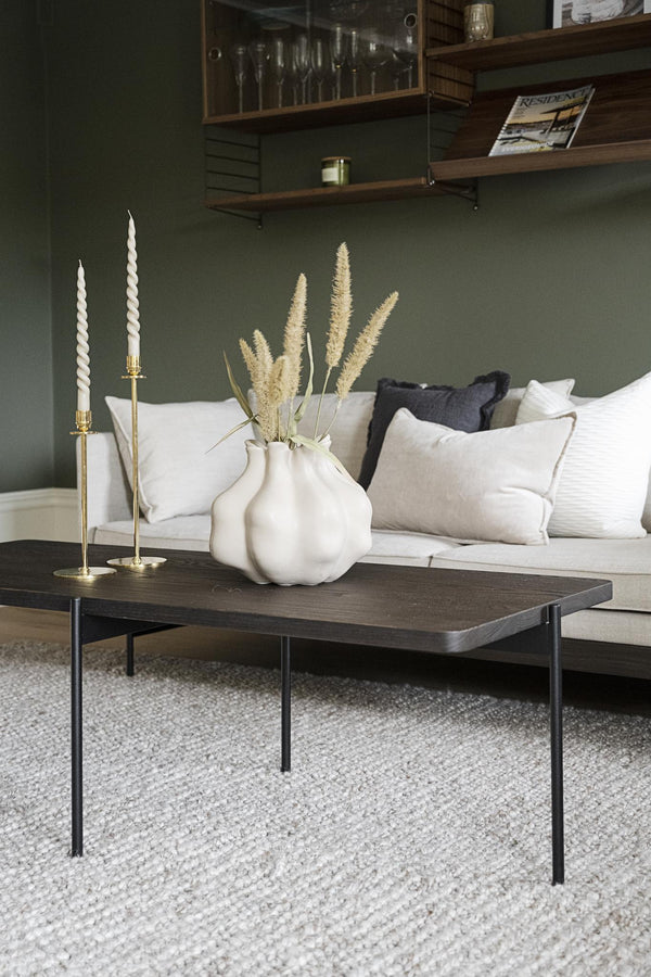 Soffbord med svart ram och mörk träskiva, dekorerat med vit vas och ljusstakar i vardagsrum med grön vägg