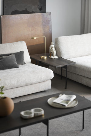 Ljust vardagsrum med beige soffor, svart soffbord, guldfärgad bordslampa och dekorativ skulptur