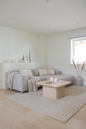 Minimalistiskt vardagsrum med grå soffa, ljust träsoffbord, beige matta och pampagräs i vas