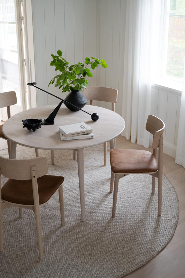 Runt matbord i ljust trä med stolar och dekorativ svart ljusstake i minimalistisk skandinavisk matsal