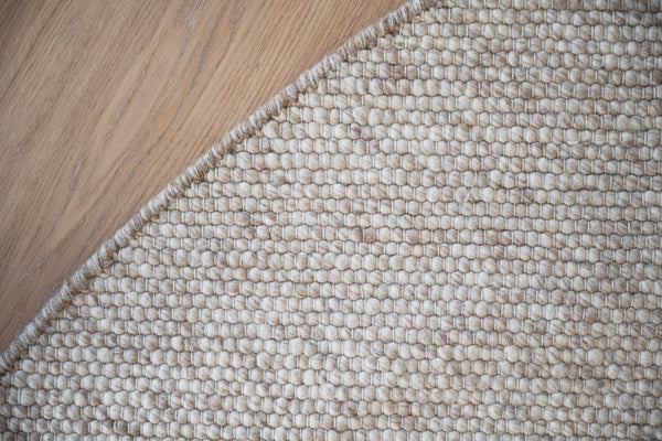 Närbild av beige matta med struktur i bomull och jute på trägolv