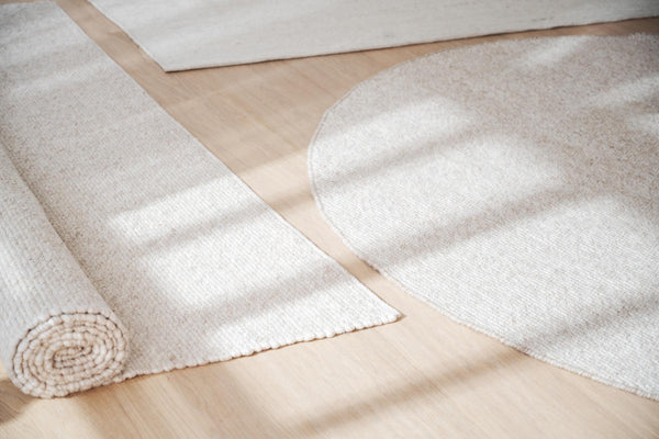 Ljusa mattor i beige och vit på trägolv, en rullad och flera utbredda