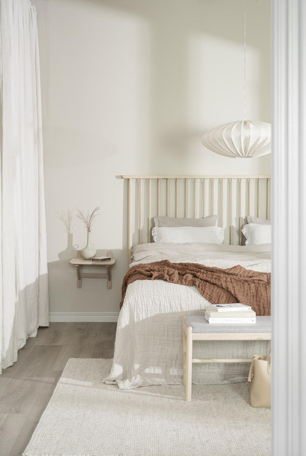 Ljust skandinaviskt sovrum med beige sänggavel, vit sängkläder och brun överkast, modern taklampa