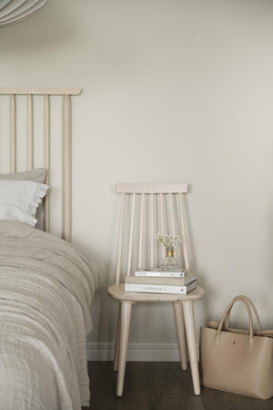 Ljust sovrum med vit spjälsäng, beige träsäng som sängbord med böcker och vas, minimalistisk inredning