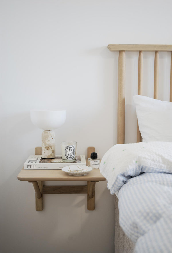 Sovrum med träsängbord, vit lampa, Diptyque doftljus och böcker i skandinavisk inredningsstil