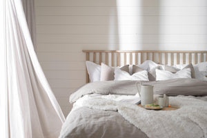 Ljust sovrum med beige sänggavel, vit och grå sängkläder, kuddar och bricka med frukost på sängen