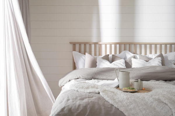 Ljust sovrum med beige sänggavel, vit och grå sängkläder, kuddar och bricka med frukost på sängen