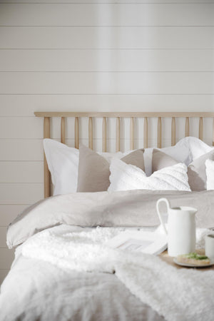 Ljust sovrum med sänggavel i naturträ, vita kuddar och sängkläder i linne, frokostbricka på sängen