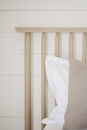 Handdukshängare i ljust trä med fem rundade pinnar och vit handduk mot vit vägg