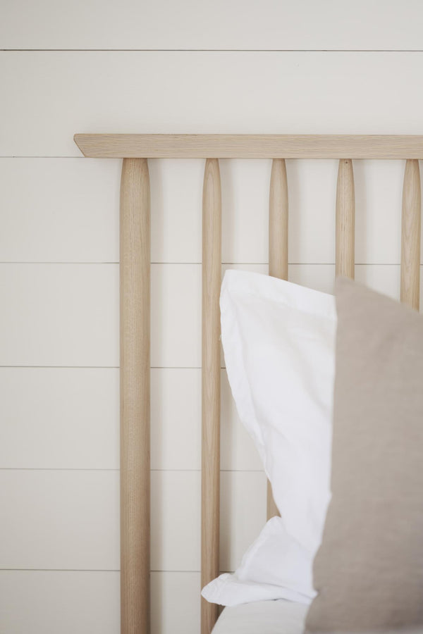 Handdukshängare i ljust trä med fem rundade pinnar och vit handduk mot vit vägg