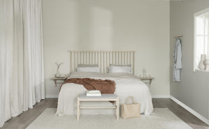 Ljust sovrum med vit sängkläder, beige sänggavel i trä, brun pläd och minimalistisk inredning i naturliga toner