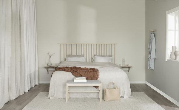 Ljust sovrum med vit sängkläder, beige sänggavel i trä, brun pläd och minimalistisk inredning i naturliga toner