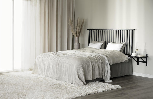 Sovrum i neutrala toner med svart spjälsäng, ljusgrå textilier och fluffig matta på mörkt trägolv