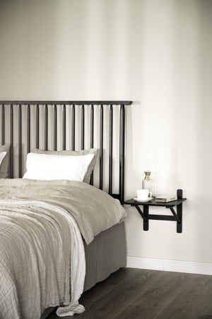 Sovrum med svart ribbat sänggavel, beige sängkläder och väggmonterat sängbord i minimalistisk stil