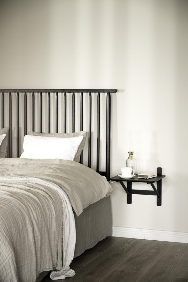 Sovrum med svart ribbat sänggavel, beige sängkläder och väggmonterat sängbord i minimalistisk stil