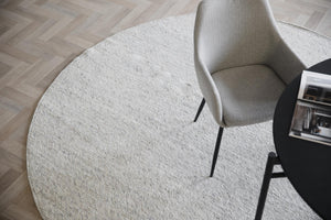 Rund ljusgrå matta med beige stol och svarta ben på parkett i herringbone-mönster