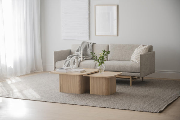 Beige soffbord i trä med räfflad design framför grå soffa i minimalistiskt vardagsrum med ljus matta