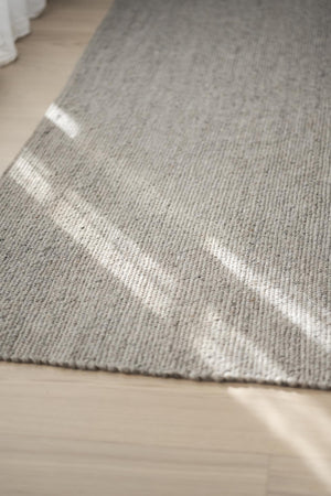 Grå matta med vita ränder i närbild på trägolv, visar mattans textur och vävning