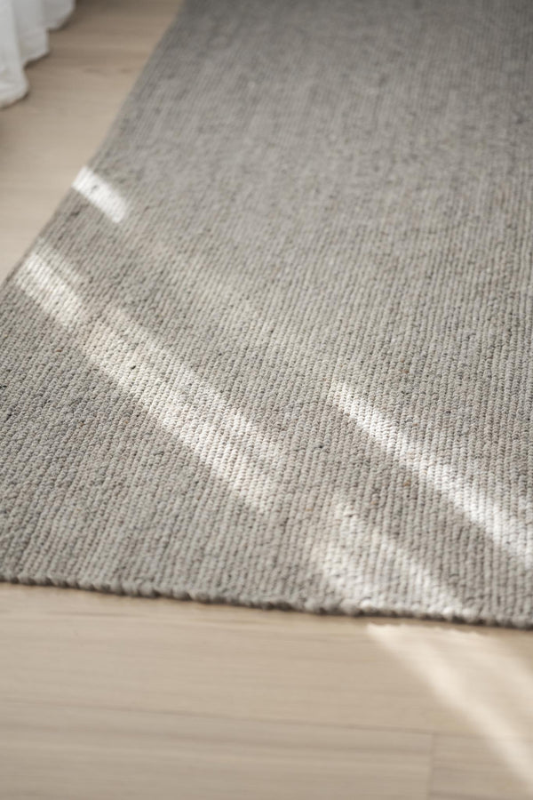 Grå matta med vita ränder i närbild på trägolv, visar mattans textur och vävning