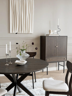 Matbord i mörkt trä med korsben, sideboard med ribbad front och dekorativa ljusstakar i elegant matsal