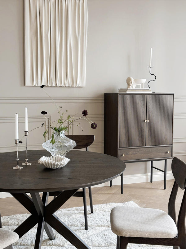 Matbord i mörkt trä med korsben, sideboard med ribbad front och dekorativa ljusstakar i elegant matsal